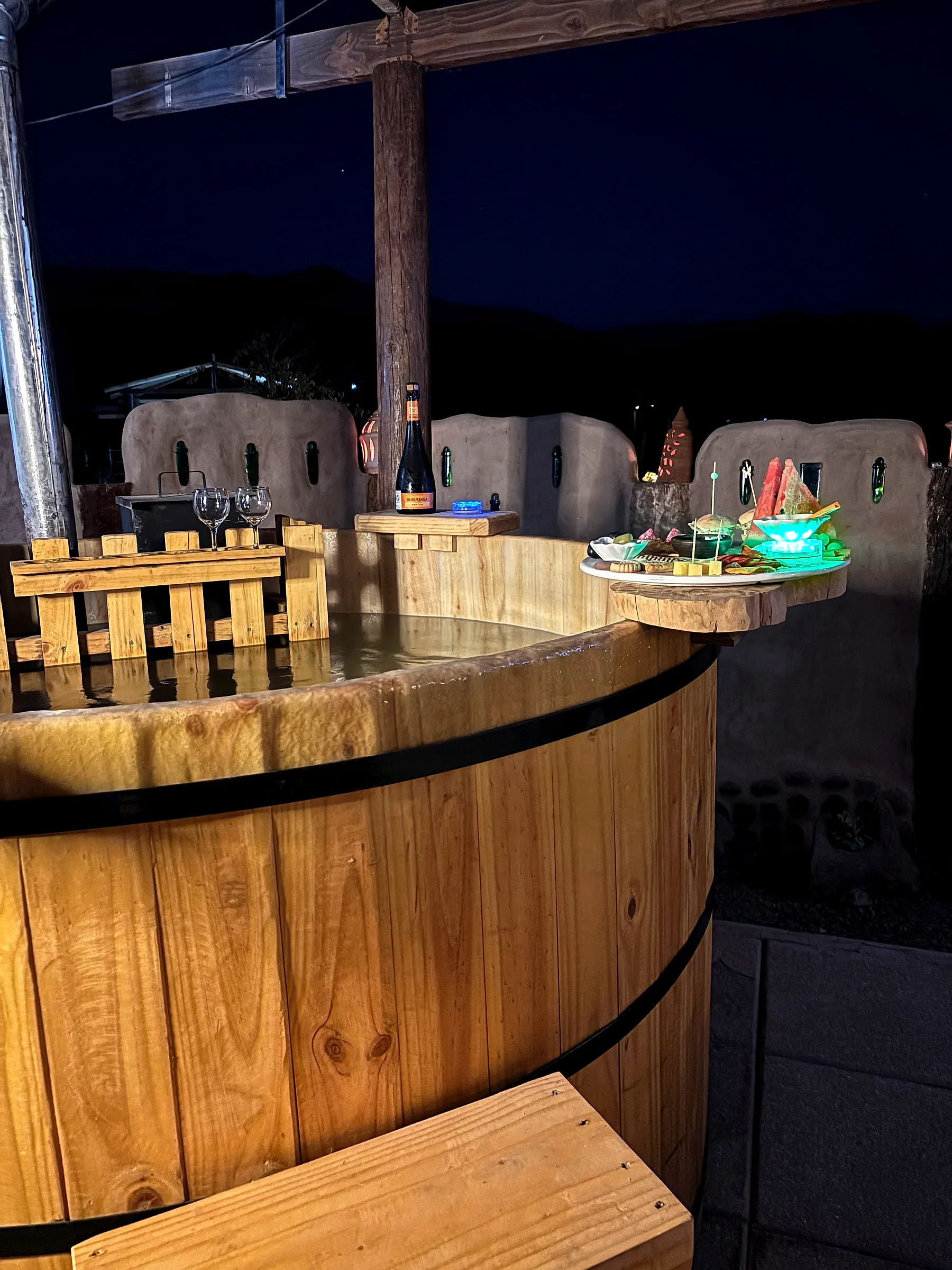 Tinaja de madera con agua caliente de noche, con las montañas del Atacama al fondo